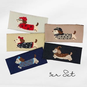 Könnte beinhalten: Fünf gestickte Aufnäher mit Dackel-Hunden in verschiedenen Outfits. Jeder Aufnäher hat eine rechteckige Form mit beigem, hellbraunem, marineblauem oder schwarzem Hintergrund. Die Hunde tragen Pullover, Hüte und Brillen. Der Text "5er Set" ist kursiv geschrieben.