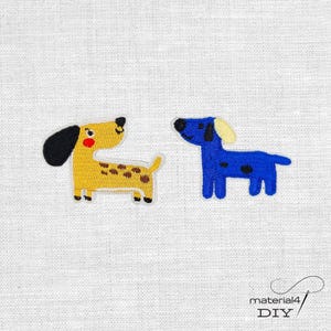 Könnte beinhalten: Zwei gestickte Dackel-Patches. Einer ist gelb mit braunen Flecken, einem schwarzen Ohr und einem gelben Schwanz. Der andere ist blau mit einem gelben Ohr. Beide haben schwarze Flecken und befinden sich auf weißem Hintergrund. Der Text "material4 DIY" befindet sich unten rechts.