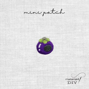 Könnte beinhalten: Ein kleiner gestickter Aufnäher, der eine violette Mangostanfrucht mit grünem Stiel und weißen Highlights zeigt. Der Text "mini patch" steht über dem Design und der Text "material4 DIY" befindet sich in der unteren rechten Ecke.