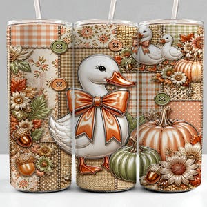 Könnte beinhalten: Ein zylindrischer Becher mit einem Patchwork-Design, das eine weiße Ente mit einer orangefarbenen Schleife, Kürbisse, Sonnenblumen, Eicheln und Knöpfe zeigt. Das Muster enthält Karomuster und Punkte in Orange-, Grün- und Beigetönen.