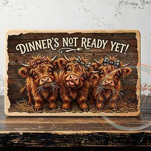 Könnte beinhalten: Ein rechteckiges Holzschild mit dem Text "DINNER'S NOT READY YET!" zeigt drei Highland-Kühe mit Schleifen. Die Kühe sind braun mit langem Fell und stehen auf Heu. Der Hintergrund ist ein Holzmaserungsmuster.
