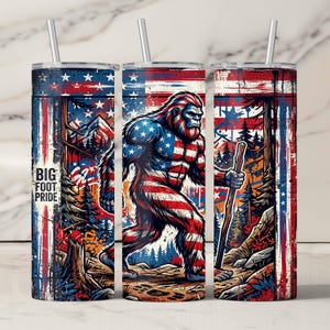 Könnte beinhalten: Drei Edelstahlbecher mit Strohhalmen. Jeder Becher zeigt ein Design von Bigfoot in den Farben der amerikanischen Flagge: Rot, Weiß und Blau. Auf einem Becher steht der Text "BIG FOOT PRIDE". Der Hintergrund zeigt Bäume und Berge.