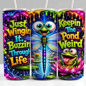 May include: A cylindrical tumbler with a straw featuring a vibrant, multi-colored design of a dragonfly and a frog on a lily pad. The text reads Just Wingin It, Buzzin Through Life and Keepin The Pond Weird against a background of dripping neon paint.