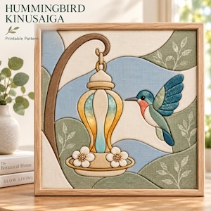 Puede incluir: Una pieza de arte Kinusaiga enmarcada de forma cuadrada que muestra un colibrí cerca de un comedero colgante. El diseño utiliza texturas de tela en tonos azul, verde y crema, con detalles florales blancos en la base y un marco de madera clara.
