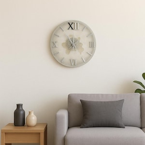 May include: A round, light gray wall clock with Roman numerals and black hands. The clock has a distressed, vintage look and is mounted on a cream-colored wall. A gray sofa with a gray pillow and a wooden side table with vases are in the foreground.