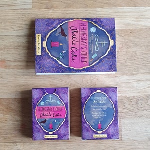 May include: A set of oracle cards with a purple and gold design. The cards feature a black crow, a candle, and a symbol. The box for the cards has the text "Wednesday's Child Oracle Cards" on the front.
