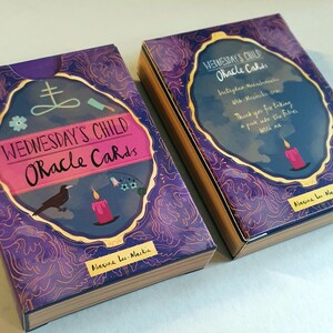 May include: Two boxes of Wednesday's Child Oracle Cards. The boxes are purple with gold accents and feature a black crow, a lit candle, and a pentagram. The text on the boxes reads "Wednesday's Child Oracle Cards" and "Maxine Lee-Mackie".