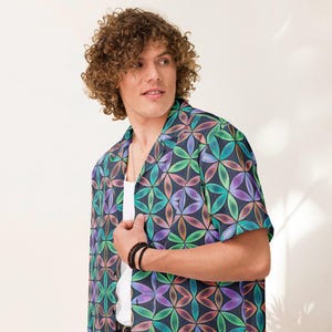 Op de afbeelding: Een shirt met korte mouwen met een kleurrijk bloemenpatroon in tinten paars, groen en blauw. Het shirt heeft een donkerblauwe achtergrond en een klassieke kraag. Het wordt gedragen over een wit ondershirt.