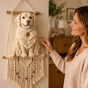 Könnte beinhalten: Ein cremefarbener, gehäkelter Golden Retriever als Wandbehang, der an zwei horizontalen Holzstäben befestigt ist. Die Hundefigur trägt eine herzförmige Marke mit der Aufschrift GOLDEN HEART. Das Stück ist mit Makramee-Fransen und Holzperlen verziert.