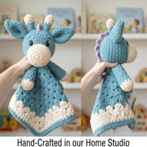 Könnte beinhalten: Eine handgefertigte Sicherheitsdecke mit einer gehäkelten Giraffe in Blau und Creme. Die Giraffe hat große Ohren, eine cremefarbene Schnauze und eine lila Mähne. Die Decke hat eine quadratische Form mit einem cremefarbenen, gewellten Rand. Text: Hand-Crafted in our Home Studio.