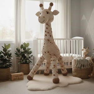 Könnte beinhalten: Eine große, handgefertigte Häkelgiraffe in einem Kinderzimmer. Die Giraffe ist beige mit braunen Flecken und Akzenten. Sie steht auf einem weißen, wolkenförmigen Teppich. Das Kinderzimmer hat ein Kinderbett, Pflanzen und einen Korb mit einer kleineren Giraffe.
