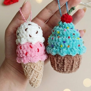 Könnte beinhalten: Zwei gehäkelte Plüsch-Ornamente in Form einer Eiswaffel und eines Cupcakes. Die Eiswaffel hat eine beige Waffelbasis, eine rosa Kugel und eine weiße Spitze mit braunen Streuseln. Der Cupcake hat eine braune Basis, blaues Frosting und bunte Perlen.