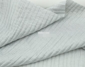 May include: A light gray fabric featuring a distinct crinkled texture with vertical ribbed lines running throughout the material. The textile is draped in soft folds, highlighting the consistent puckered pattern across the entire surface.