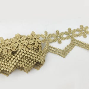 May include: Gold lace trim with a delicate floral pattern. The trim features a repeating design of small flowers and a scalloped edge.
