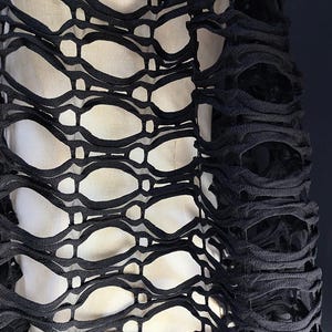 Puede incluir: Tela negra con un patrón tejido de trama abierta. La tela tiene un aspecto texturizado y ligeramente deshilachado.