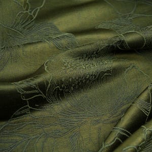 Pode incluir: Close-up de tecido verde-oliva com um padrão floral. O tecido tem um brilho sutil e é drapeado, mostrando a textura e o design. O padrão floral é em um tom de verde mais escuro, criando um contraste.