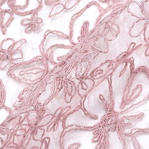 May include: Close-up of a delicate, light pink floral lace fabric. The lace features embroidered flowers and swirling patterns, creating a textured and elegant design. The fabric is semi-transparent, with a subtle sheen, perfect for apparel and craft projects.
