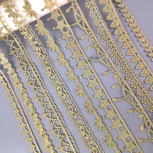 Könnte beinhalten: Sortiment aus goldener Spitzenborte mit verschiedenen Mustern und Designs. Die Spitze ist zart und filigran, mit einem schimmernden Metallic-Finish.