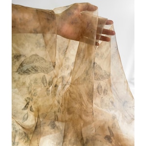 May include: A sheer fabric with a beige background and a pattern of dark brown leaves. The fabric is translucent and has a delicate, flowing texture.