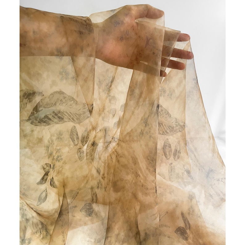 May include: A sheer fabric with a beige background and a pattern of dark brown leaves. The fabric is translucent and has a delicate, flowing texture.