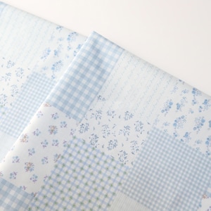 Könnte beinhalten: Zwei überlappende Stoffstücke mit Patchwork-Design. Die Muster umfassen Vichy, Blumendrucke und Schriftzüge in Blau und Weiß. Der Stoff scheint aus Baumwolle oder einem ähnlichen leichten Material zu sein.