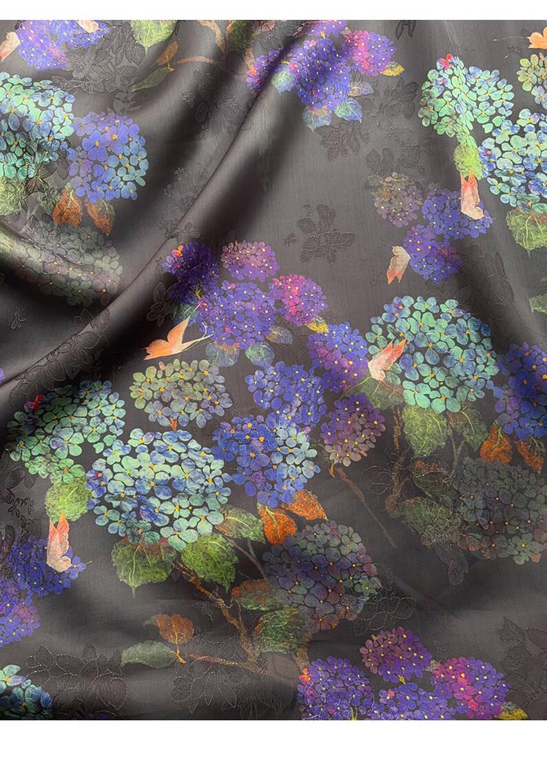 May include: Dark grey fabric with a floral pattern of blue, purple, and green hydrangeas. The fabric has a subtle sheen and a detailed design, with hints of orange and pink.