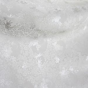 Może przedstawiać: Biała tkanina z delikatnym wzorem kwiatowym. Wzór jest wytłoczony i ma subtelny połysk.