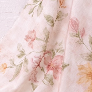 May include: A lightweight, semi-sheer fabric featuring a soft, pale pink background with a delicate watercolour-style floral print. The pattern displays various blooming flowers in shades of muted pink, soft yellow, and sage green foliage.