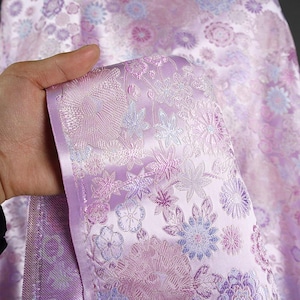Puede incluir: Primer plano de una tela morada con un patrón floral. La tela tiene un brillo sutil y está estampada con un diseño en relieve.