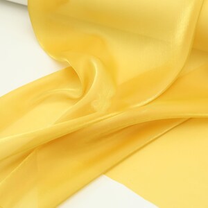Könnte beinhalten: Nahaufnahme eines fließenden, goldgelben Stoffes. Das Material scheint transparent zu sein, mit leichtem Glanz, und ist in weichen Falten drapiert. Die Farbe des Stoffes ist durchgehend, wodurch ein glattes, elegantes Aussehen entsteht. Ideal für Basteln, Dekorieren oder Mode.