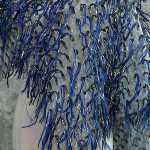 May include: Blue and gold fringe fabric with a mesh backing. The fringe is made of thin strands of yarn that are woven together to create a textured look.