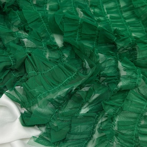 Könnte beinhalten: Nahaufnahme von smaragdgrünem, gerüschtem Tüllstoff. Der Stoff ist geschichtet und strukturiert, mit einem zarten, transparenten Aussehen. Der Tüll ist über einer weißen Oberfläche drapiert, wodurch ein Kontrast in Farbe und Textur entsteht. Ideal für Bastel-, Mode- oder Dekorationsprojekte.