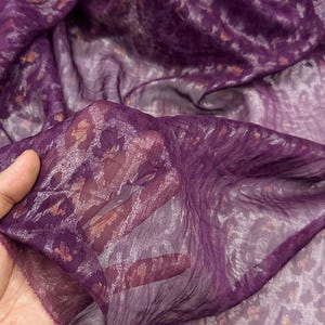 Puede incluir: Una tela transparente y fluida en tonos de morado intenso con un sutil estampado de leopardo. La tela tiene una textura arrugada y parece ligera, ideal para bufandas o prendas.
