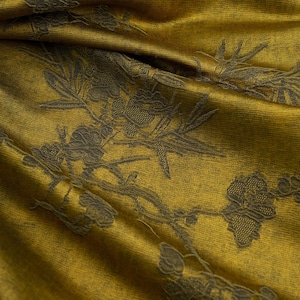 Puede incluir: Primer plano de una tela doblada con una base amarillo mostaza y un detallado estampado floral en verde oliva oscuro. El diseño presenta flores y hojas estilizadas.