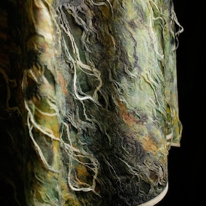 Peut inclure: Un vêtement texturé présentant un mélange chiné de tons vert forêt, olive et brun terreux. Le tissu affiche une surface fibreuse et superposée avec des fils lâches et pendants, un aspect effiloché distinct et une bordure claire unie.