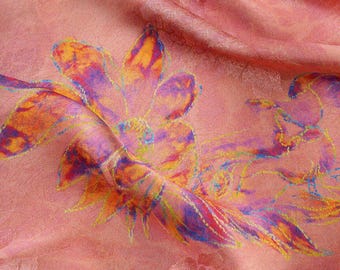 May include: A soft pink fabric featuring a large, vibrant floral print in shades of orange, purple, and blue. The material has a subtle, tone-on-tone woven pattern throughout, with folds creating depth and texture across the surface.