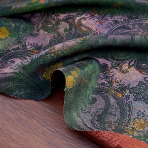 Peut inclure: Gros plan sur un tissu plié avec un motif cachemire. Le tissu présente un mélange de couleurs, notamment des verts profonds, des violets et des touches d'or. Le motif cachemire est complexe et détaillé, avec des éléments floraux et courbes.