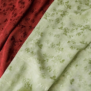 May include: A close-up of two patterned fabrics. One is a deep red with a rose design, the other is light green with a similar rose pattern. The fabrics are draped, showing their texture and design. Ideal for textiles.
