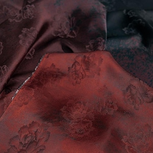 Puede incluir: Primer plano de una tela color burdeos con un patrón floral en relieve. La tela tiene una textura suave y sedosa.
