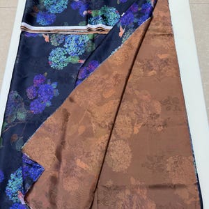 May include: Dark blue fabric with a floral design of blue and purple hydrangeas. The fabric is folded to show a brown floral patterned underside. The material is likely silk or a similar fabric.