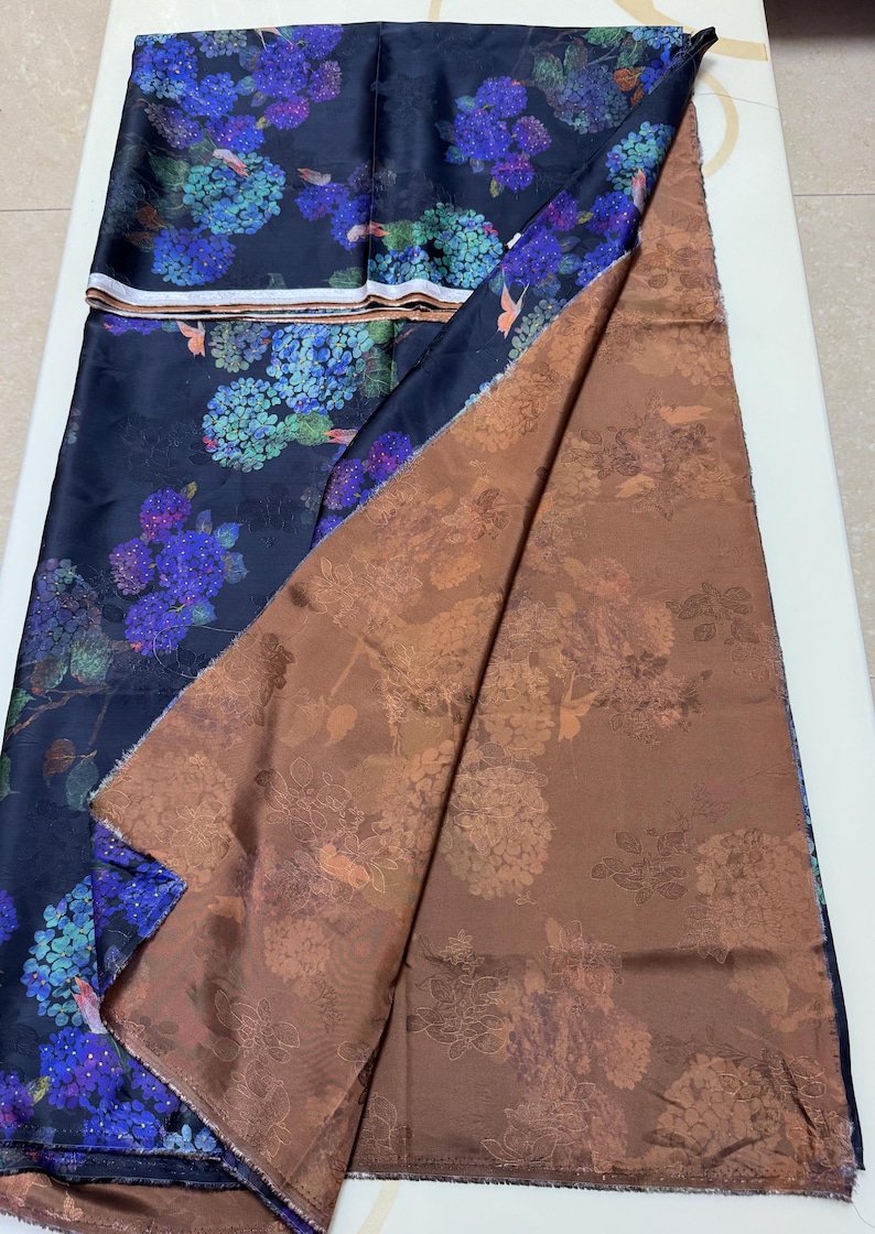 May include: Dark blue fabric with a floral design of blue and purple hydrangeas. The fabric is folded to show a brown floral patterned underside. The material is likely silk or a similar fabric.