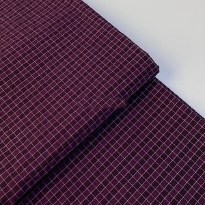 Peut inclure: Gros plan sur un tissu plié avec un motif quadrillé. Le tissu est de couleur violet foncé avec un quadrillage blanc superposé. Le tissu est plié sur lui-même, créant un effet de superposition. Le fond est blanc.