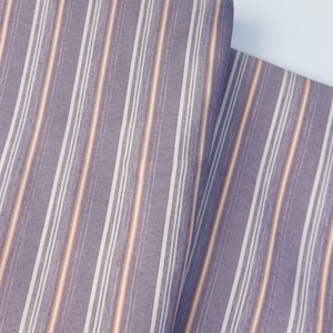 Könnte beinhalten: Nahaufnahme eines Stoffes mit Streifenmuster. Der Stoff hat vertikale Streifen in Lila, Weiß und einen dünnen orangefarbenen Streifen. Der Stoff ist gefaltet und zeigt die Textur und das Muster.