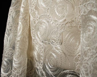 May include: A sheer off-white fabric featuring an intricate, raised embroidery pattern of swirling circular and spiral motifs. The thread work creates a textured, dimensional effect across the translucent, lightweight material.