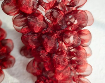 May include: Close-up of a cluster of red, semi-transparent, fabric grape-like shapes. The fabric has a slightly textured appearance, with darker red accents. The shapes are arranged in a cascading, organic form against a white background.