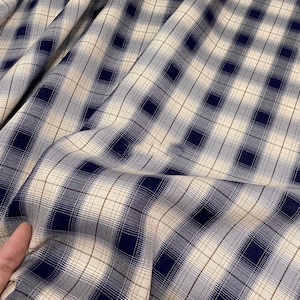 May include: A close-up of a blue and white plaid fabric. The fabric has a subtle sheen and a soft texture.