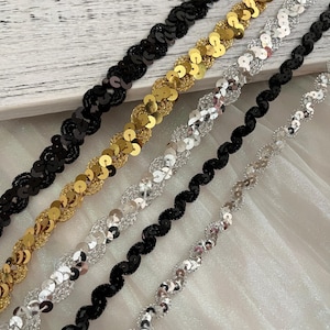 May include: Five different trims of sequined fabric in black, gold, silver, and two shades of silver. The trims are arranged in a staggered pattern, with the black trim at the top and the silver trim at the bottom.