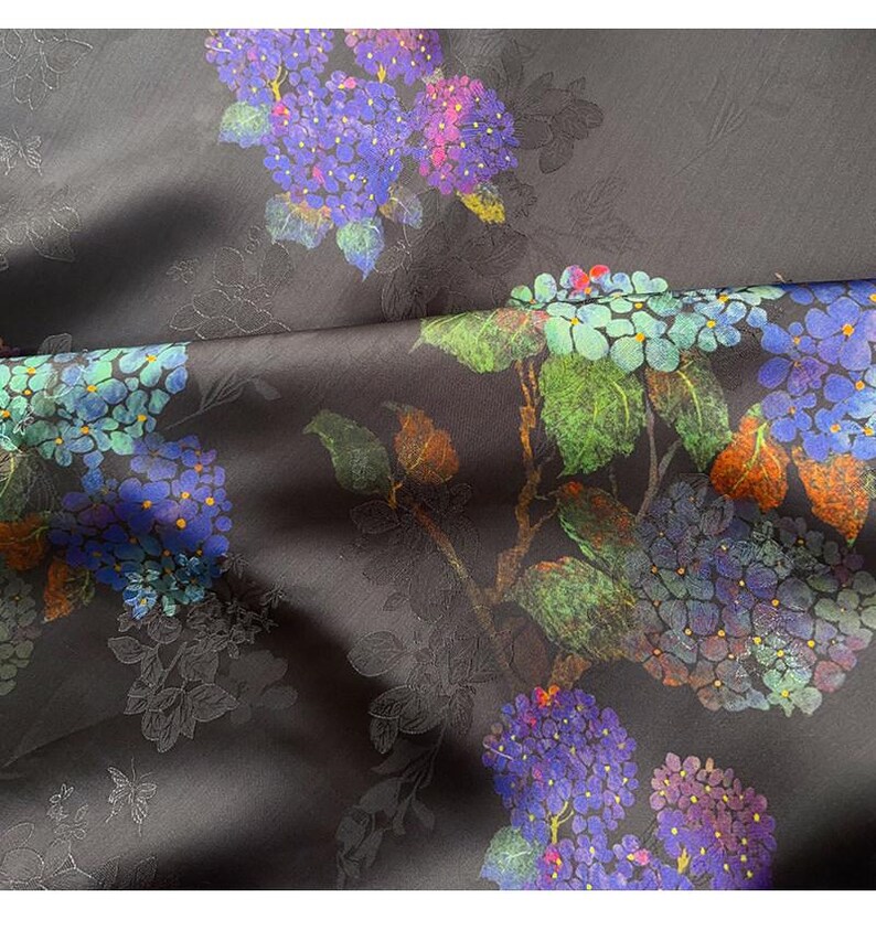 May include: Dark grey fabric with a floral design of purple, blue, and green hydrangea flowers. The material has a slight sheen and an embossed pattern of leaves and flowers. The fabric creates a rich, textured appearance.
