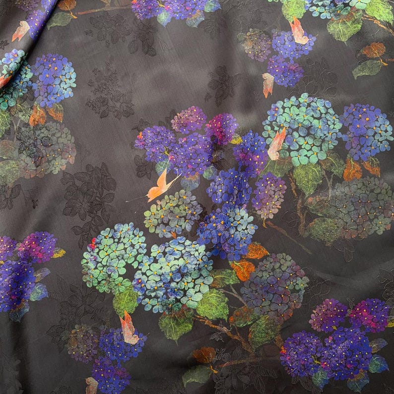 May include: Dark fabric with a floral pattern of blue, purple, and green hydrangeas. The design includes orange butterflies and green leaves against a dark background. The fabric has a subtle sheen.