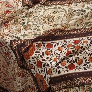 May include: Close-up of a patterned fabric with a bohemian design. The fabric features a cream background with floral and paisley patterns in shades of brown, red, and green. The design includes borders and repeating motifs.